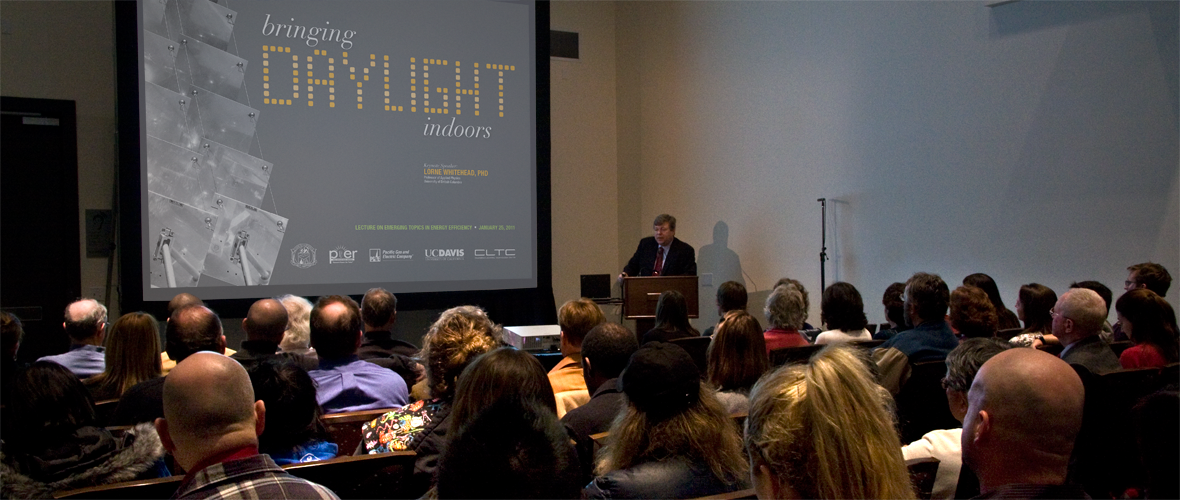 Person standing and talking at a podium in front of a group of people with a presentation that says "bringing Daylight indoors"