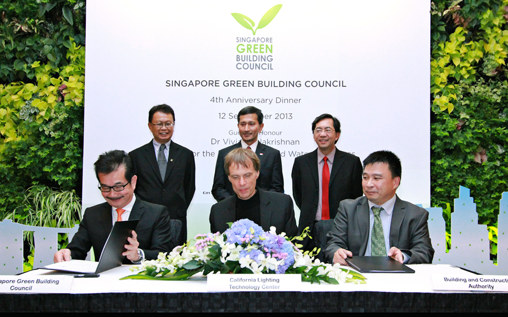 Three people sitting at a table signing formal documents with three people behind them