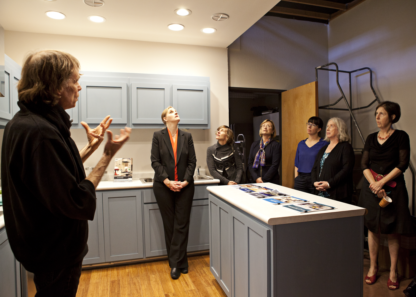 Michael Siminovitch standing and talking to a group of six people in a kitchen