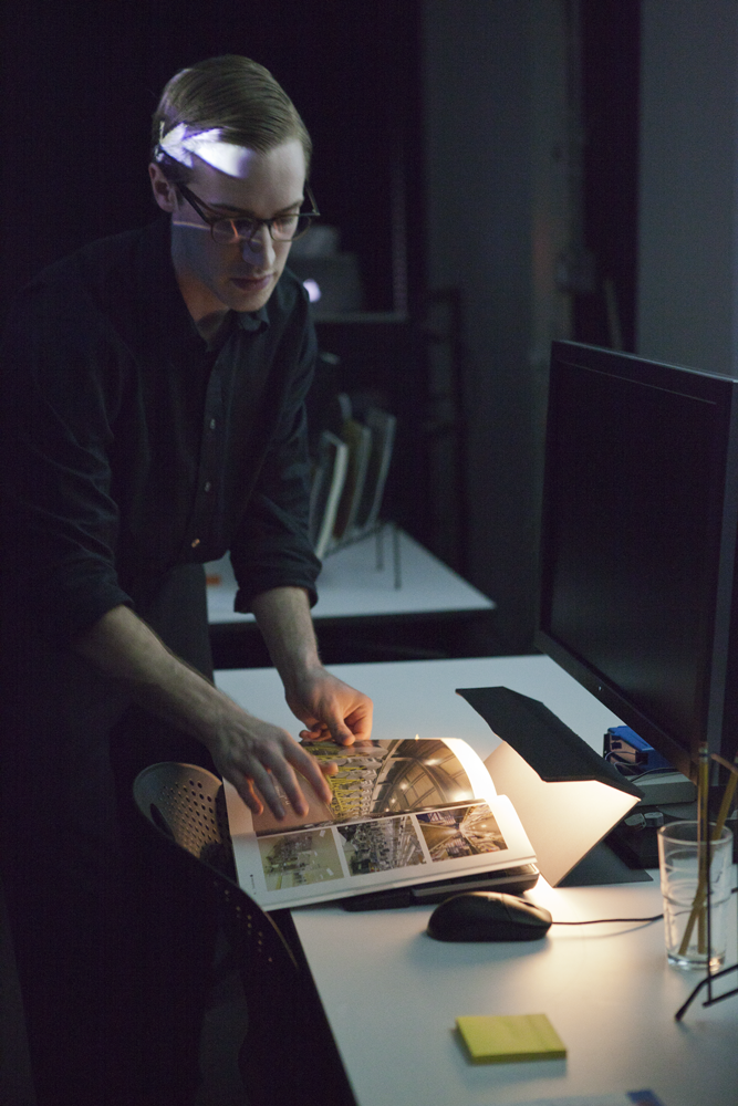 Person standing next to a desk flipping a page in a book