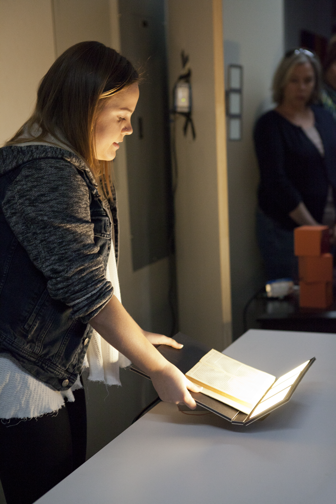 Person holding a rectangular board with three square light panels at the end to light up a piece of paper on the board 