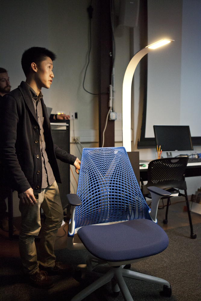 Person standing next to a chair with a light fixture that comes up and over the chair