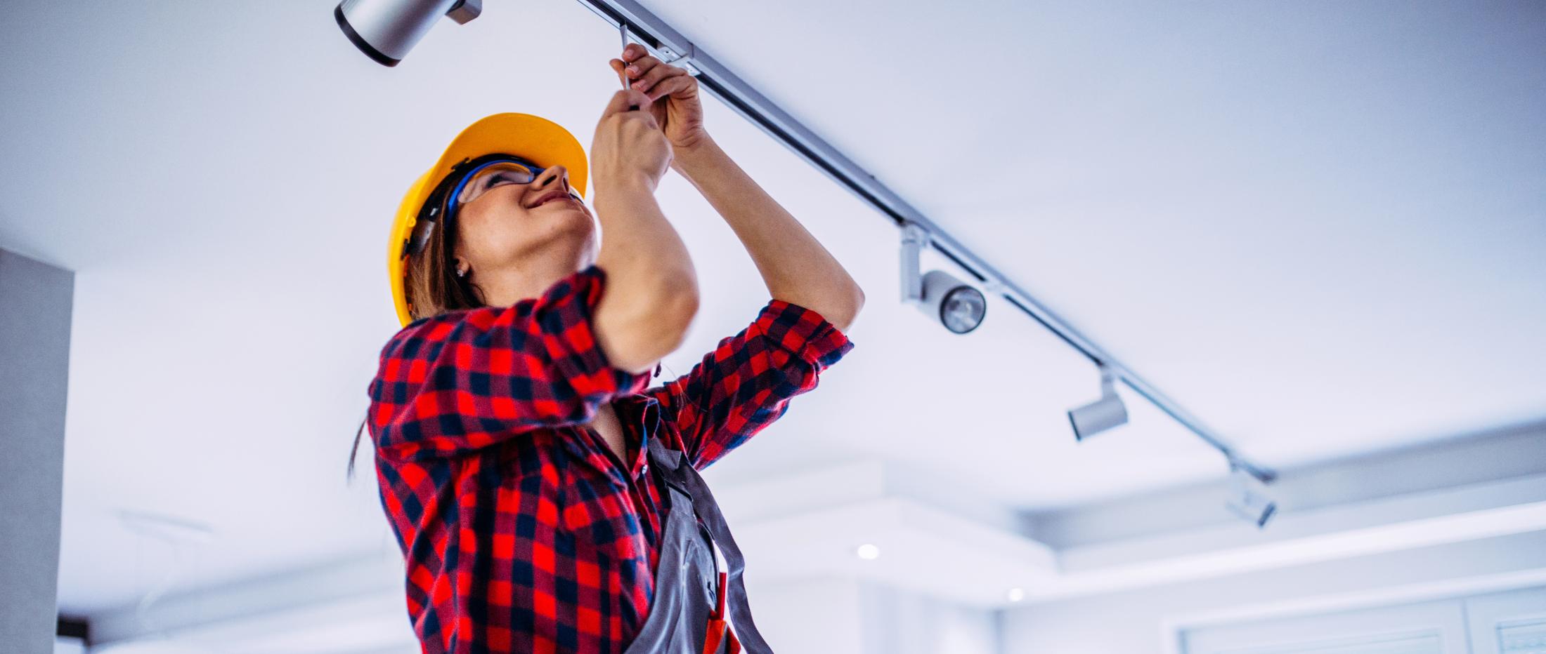 Electrician on ladder in hardhat working on overhead lighting