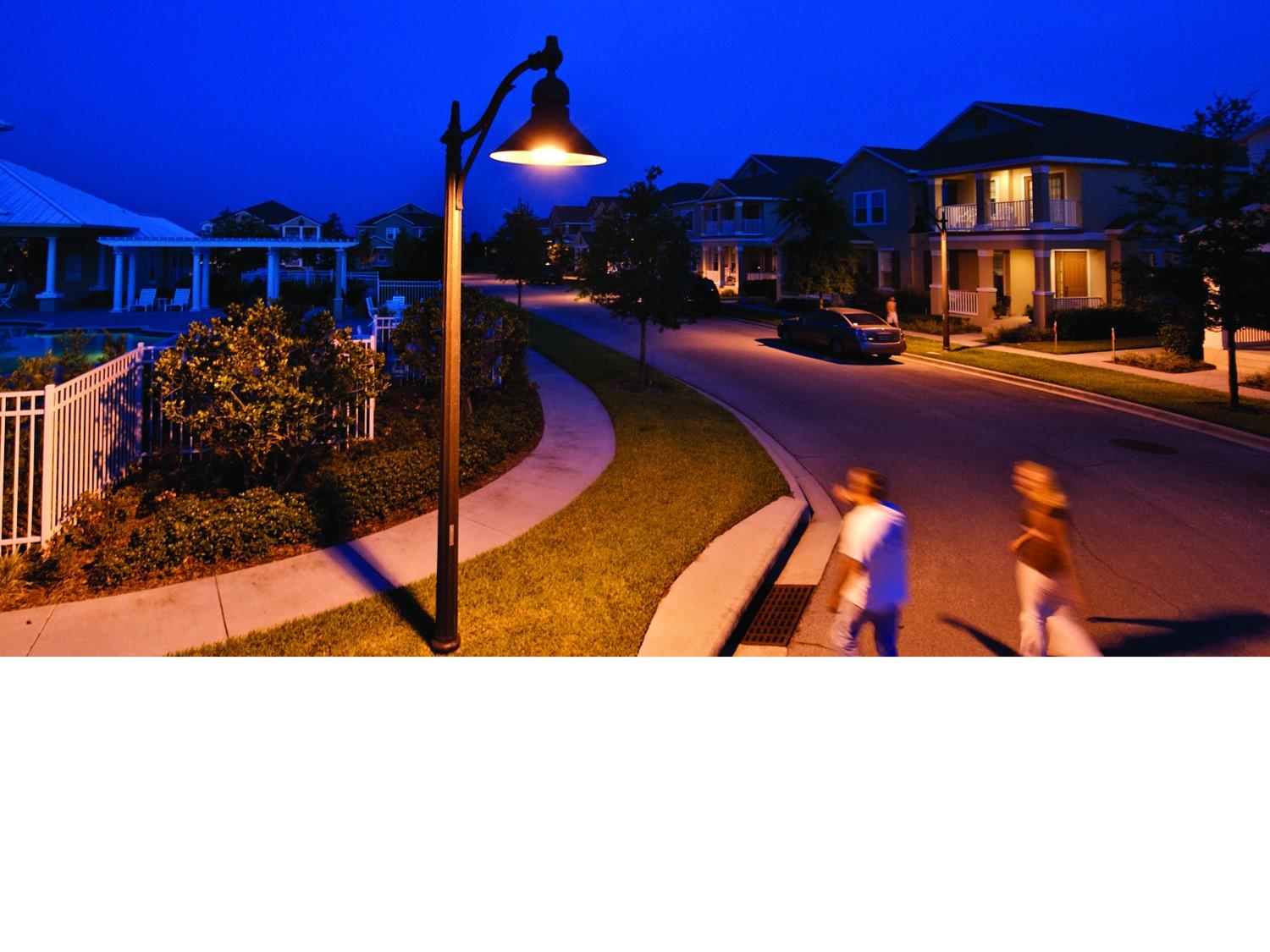 Warm residential street lighting at night with two people walking past 