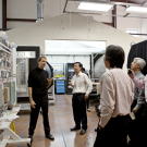 A person standing and explaining some machinery to four other people standing around them 