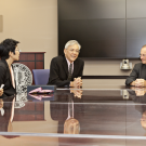 Eight people wearing formal attire sitting at a large conference room table